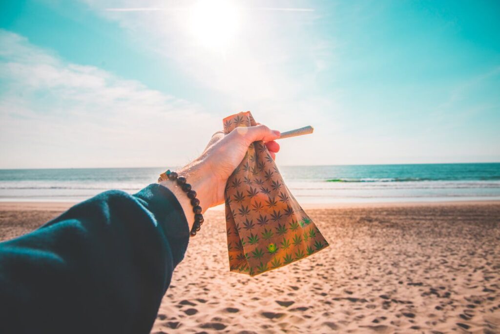 person on beach holding a marijuana joint and paper bag