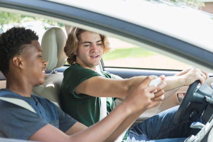 teenager driving distracted by looking at his passenger's phone