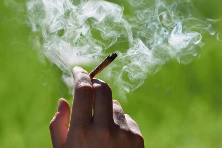 Close-Up Of A Person Smoking A Marijuana Joint Outdoors With Smoke Rising
