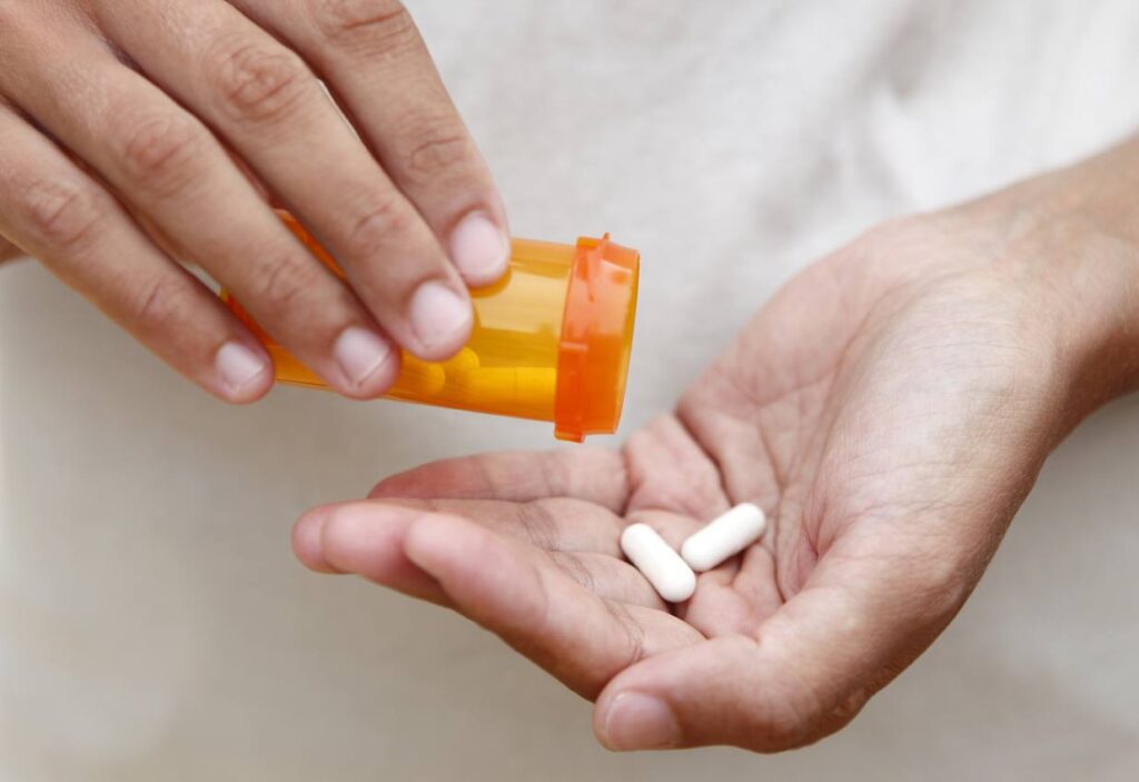 person pouring white medicine capsules from a bottle.