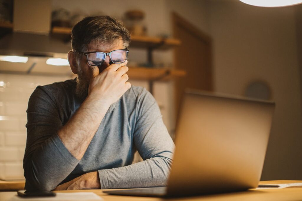 Man rubbing eyes with difficulty seeing a computer screen.