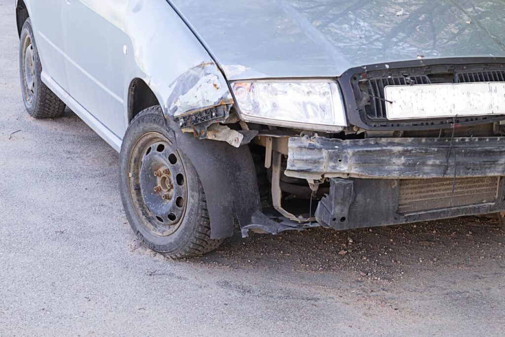 Silver car missing hubcap and front bumper after car accident 