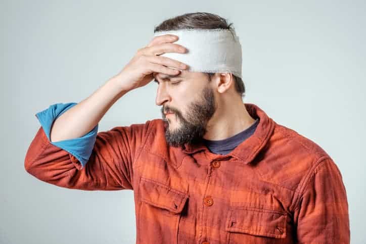man with wrapped head holding head in pain