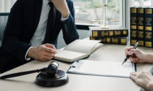 an unidentifiable bicycle accident lawyer is meeting with their client after an accident. There are law books and a gavel on their desk, with papers between them.