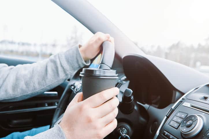 Man drinking coffee while driving the car. Driver holds black paper cup.