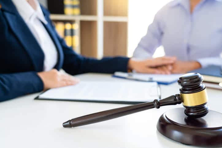 women attorney holding hands to console a client. There are papers between them, and in the corner is a gavel.