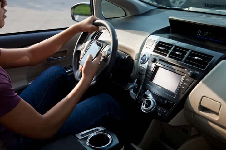 Teenage boy in driver's seat, driving and texting.