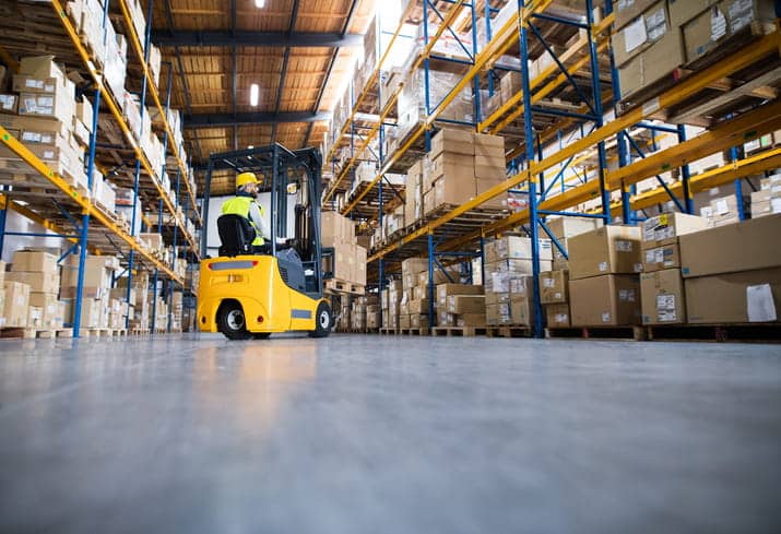 a photo taken from the ground, looking up at a yellow forklift while it stacks boxes in a warehouse aisle.
