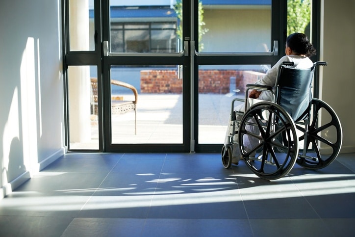 An old woman sitting in a wheelchair at the door of an institution.