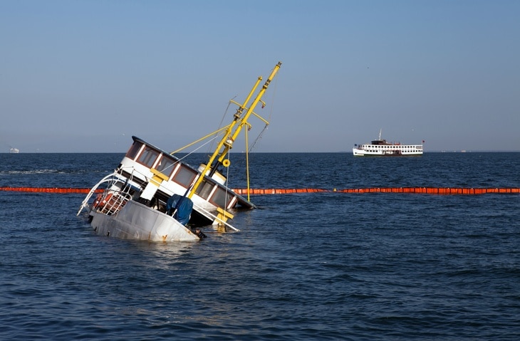 A photo of a white boat partially submerged under water, in the process of sinking. 