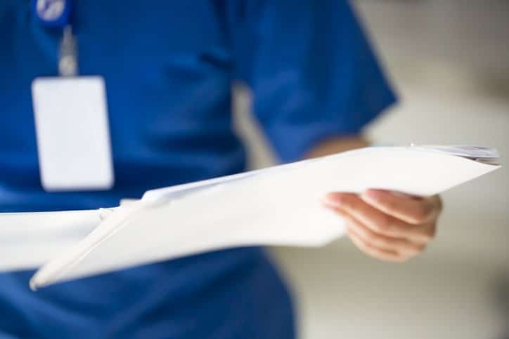 An unrecognizable nurse holding a report in their hands.