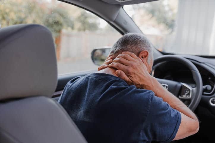 The back view of a man clutching his neck in the driver seat after suffering from car accident injuries.