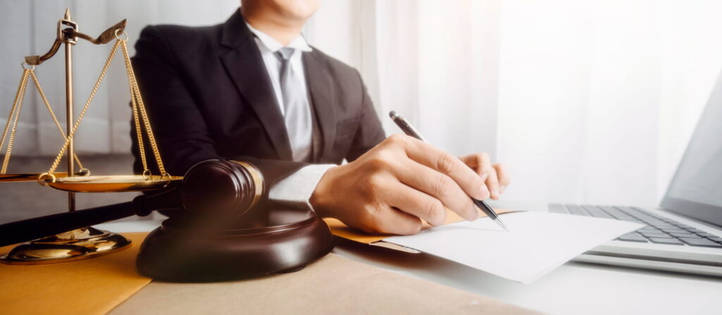 A closeup of a Miami drunk driver crash attorney at his desk, working on paperwork. There is also a laptop, the scales of justice and a gavel on his desk.