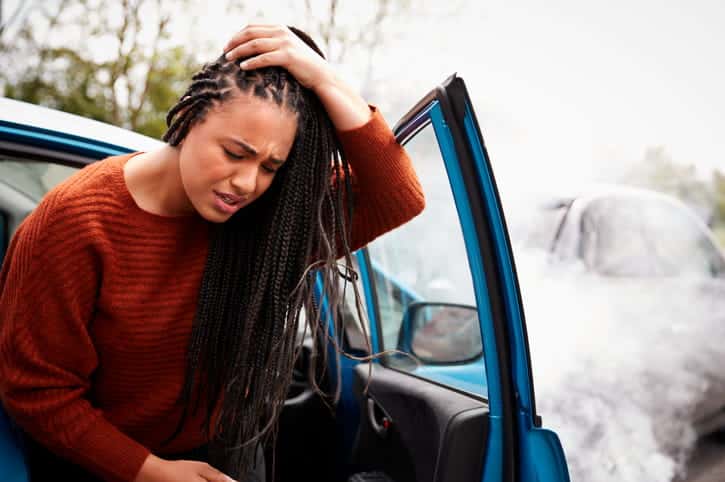 A woman holding her head in pain as she sits in her car after receiving car accident injuries.