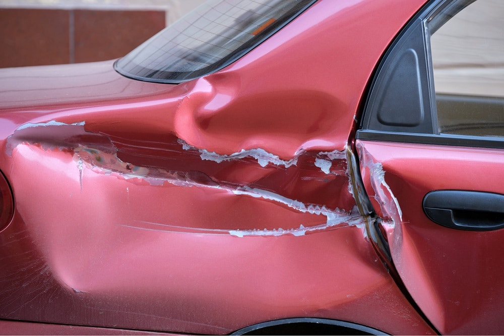 Damage to the side of a red vehicle after a hit-and-run accident.