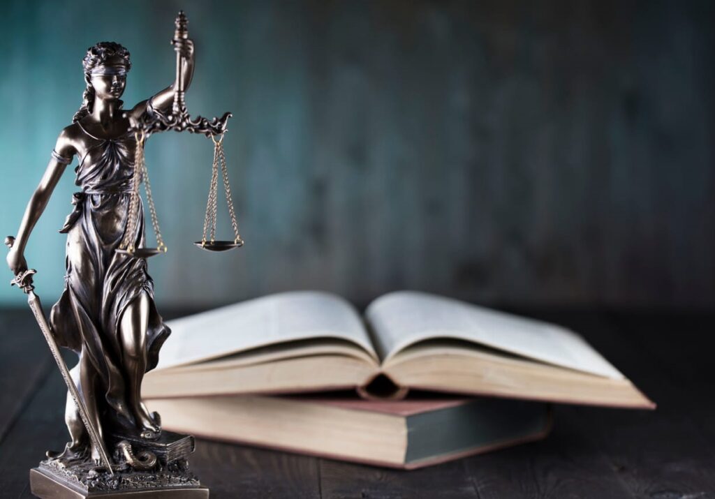 A Lady Justice statue and an open book stacked on top another book, both are sitting on a Miami’s top car accident lawyer's desk.