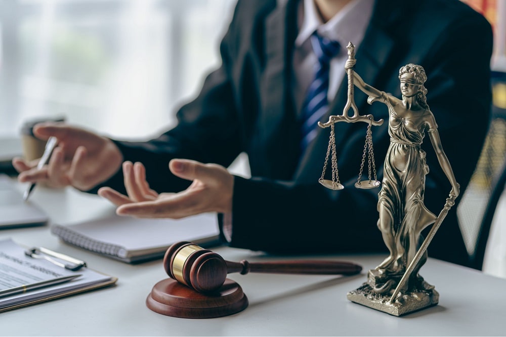 An auto accident lawyer sits at his desk, discussing his case. On his desk is paperwork, a gavel, and the Lady Justice statue.