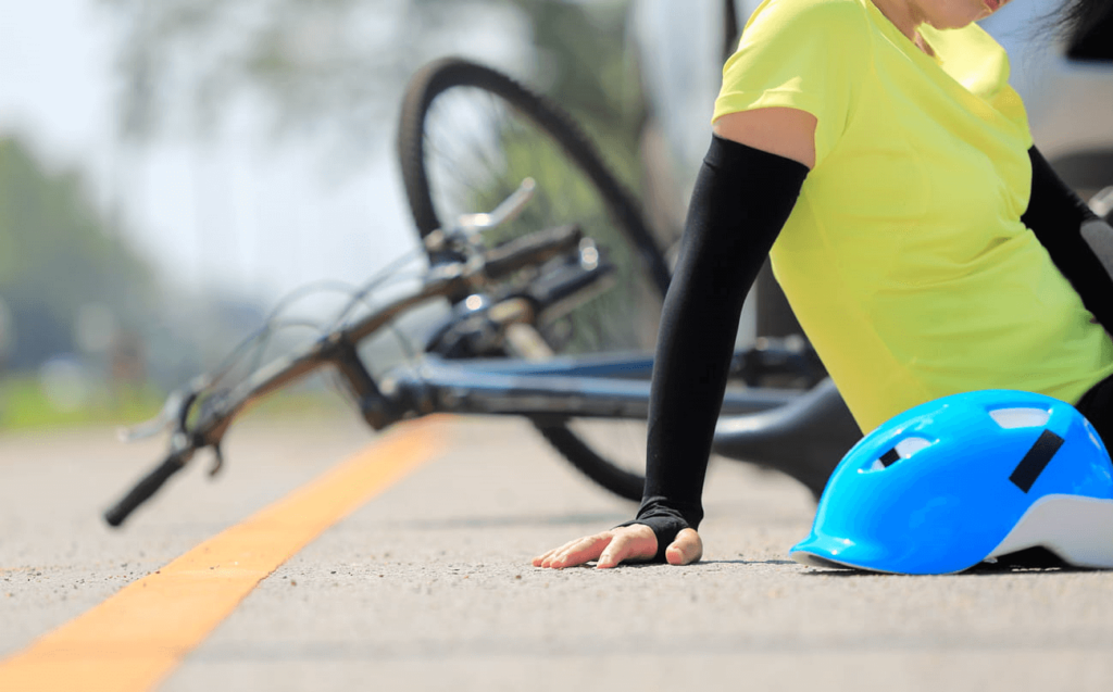 A cyclist sitting in the roadway with their bike and helmet next to them after a hit-and-run accident.