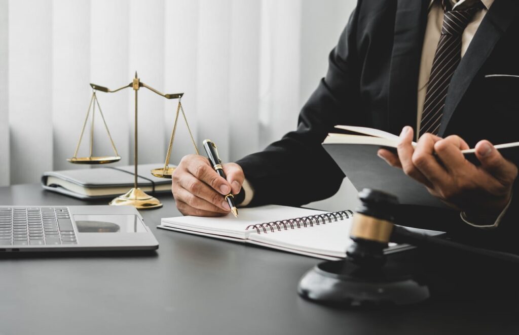 A wrongful death lawyer working at his desk. On his desk is an open laptop, a gavel, and the scales of justice.