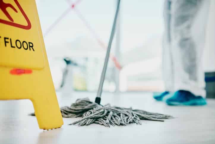 Wet floor sign with person mopping in background