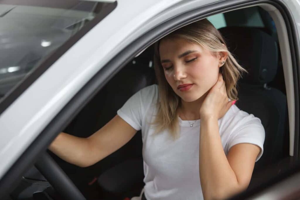 Woman holding her neck in pain sitting in a car.
