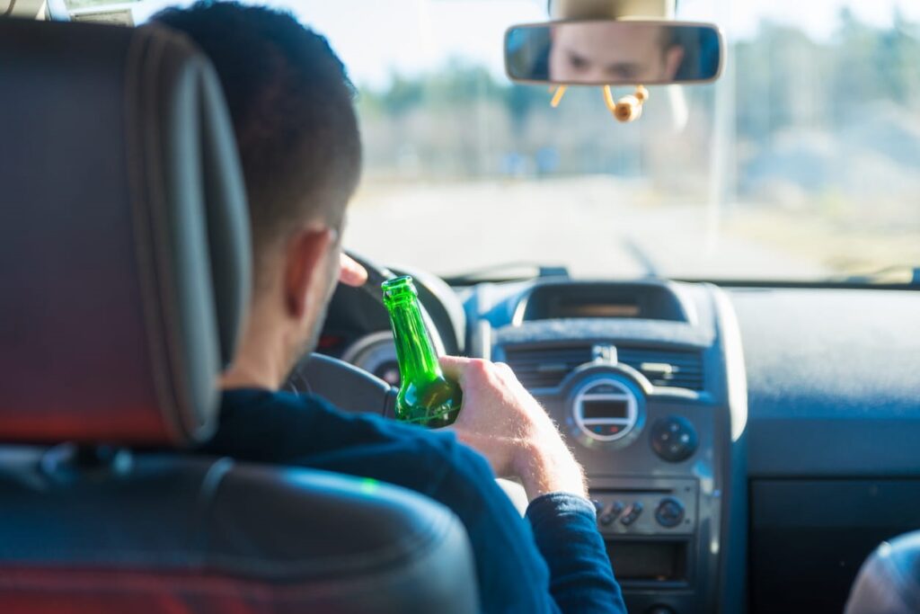 A man drinking behind the wheel while driving.