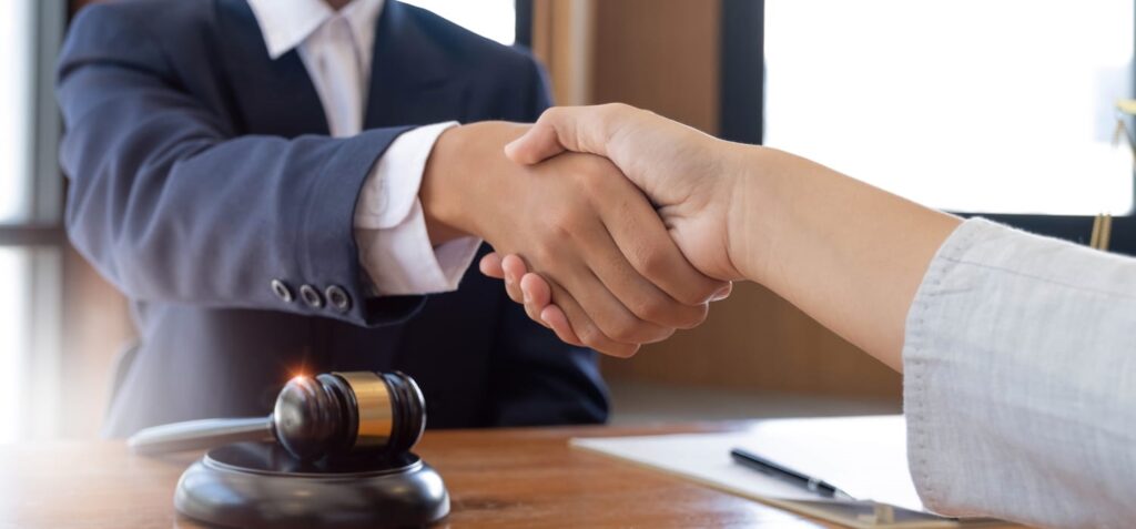 A personal injury lawyer shaking hands with their client. On their desk is paperwork and a gavel.