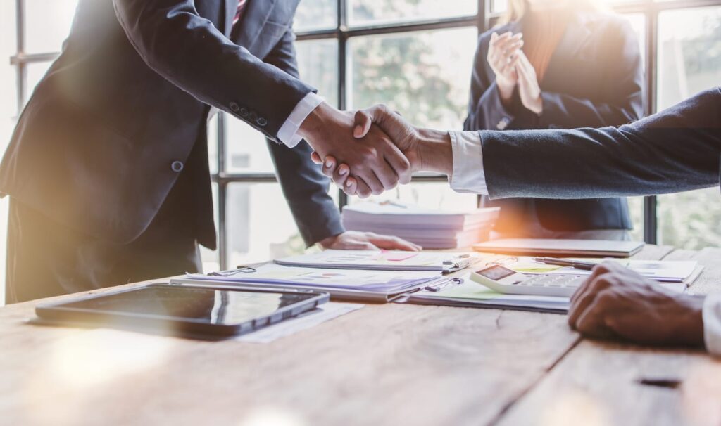 A wrongful death attorney in Miami, FL, shaking hands with their client. In front of them on the table is paperwork.