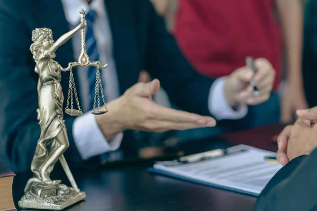 A personal injury lawyer working at his desk with a client. Next to him is a Lady Justice statue.