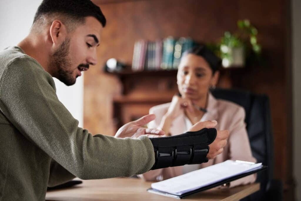 A personal injury lawyer reviews paperwork with her injured client. He has a wrist brace on.