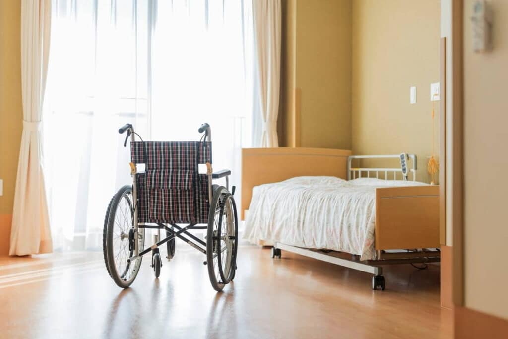 An empty room in a nursing home with a wheelchair and a bed