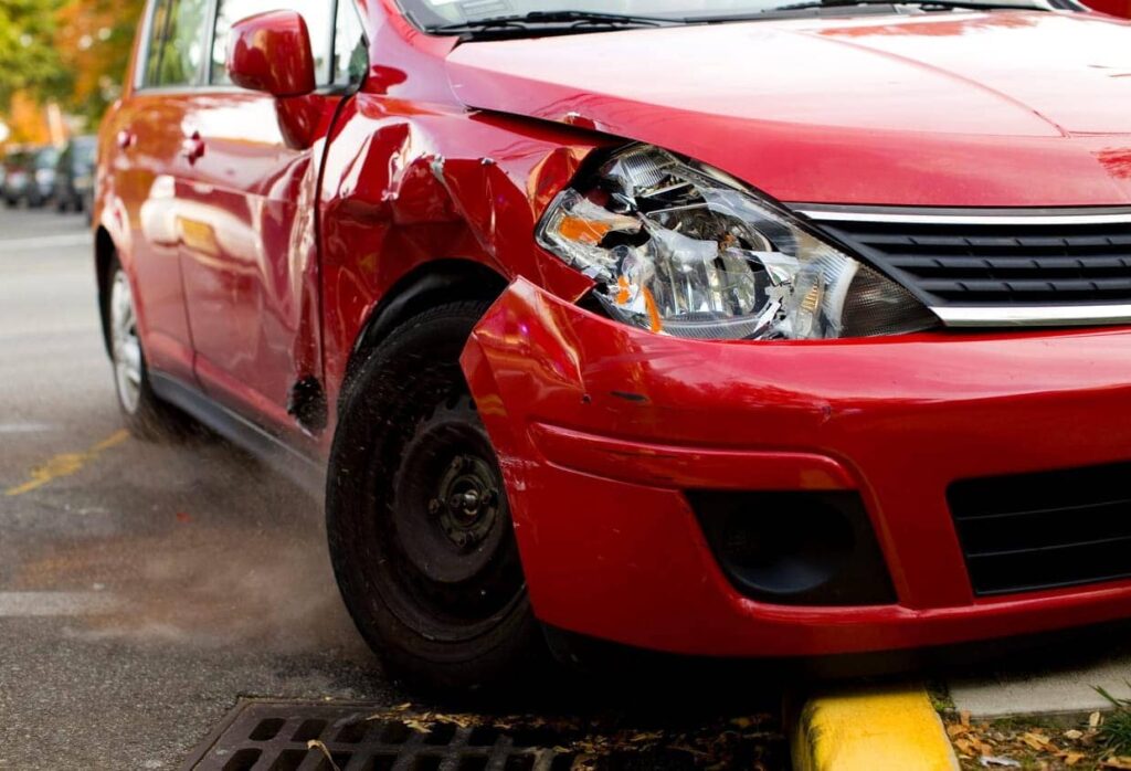 A red vehicle badly damaged in the front end after a rideshare car accident. 