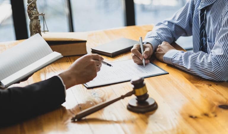 A car accident lawyer assisting his client at his desk. Between them is paperwork, a gavel, and books.