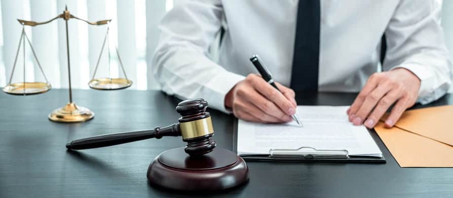 A personal injury attorney working on paperwork at their desk. Next to them is a gavel and the scales of justice.
