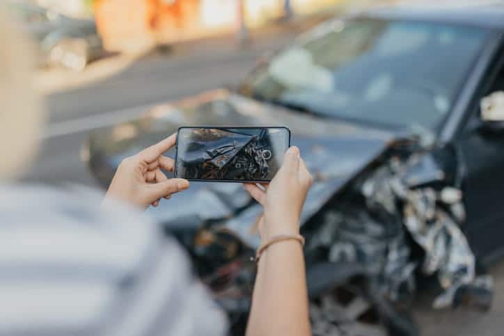 A person documenting the severe damage of their vehicle with their smart phone after an accident. 