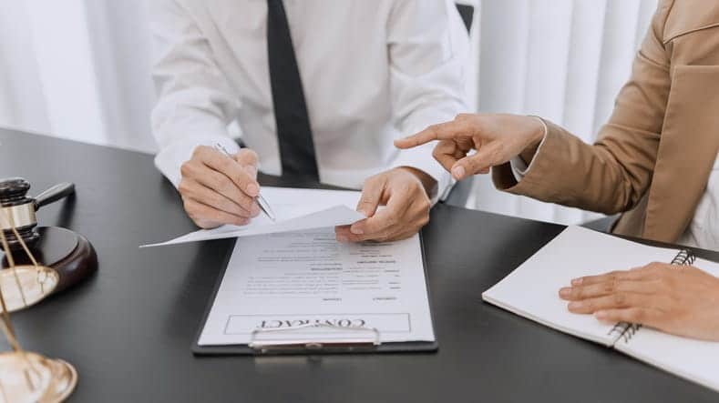 A car accident lawyer reviewing a contract with his client. Next to him is the scales of justice and a gavel.