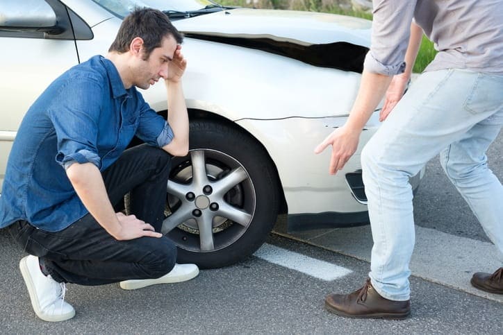 A man kneeling next to his car after an accident