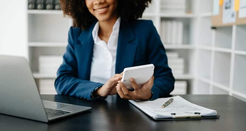 A personal injury lawyer using a calculator at her desk. In front of her is paperwork and an open laptop.