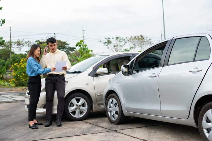 Two people reviewing paperwork outside of their vehicles after being in a car accident. 