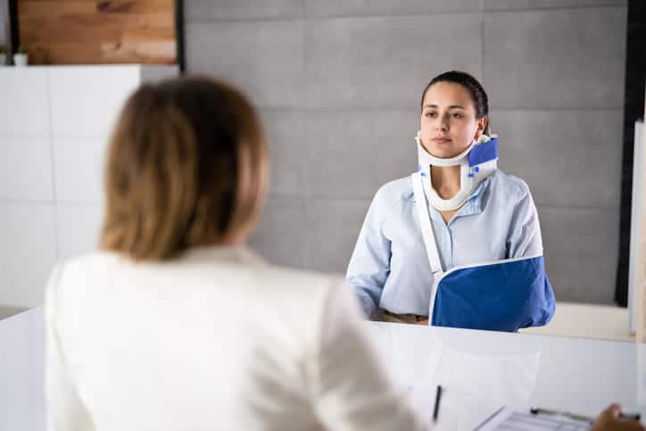 An injured client in a neck brace and an arm sling speaking with her personal injury attorney. 