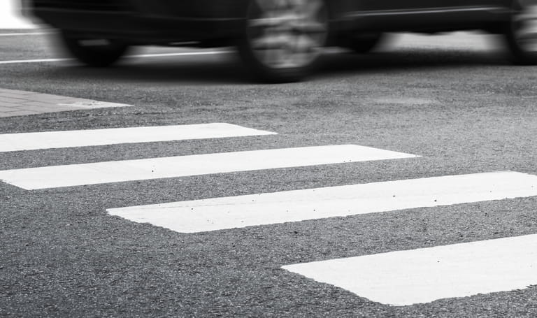 A pedestrian cross walk with a car speeding past