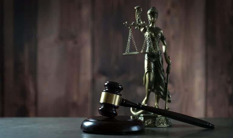 A gavel sits in front of a Lady Justice statue. 