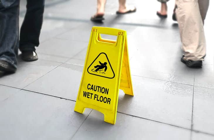 A yellow caution: wet floor sign propped up as people walk by.