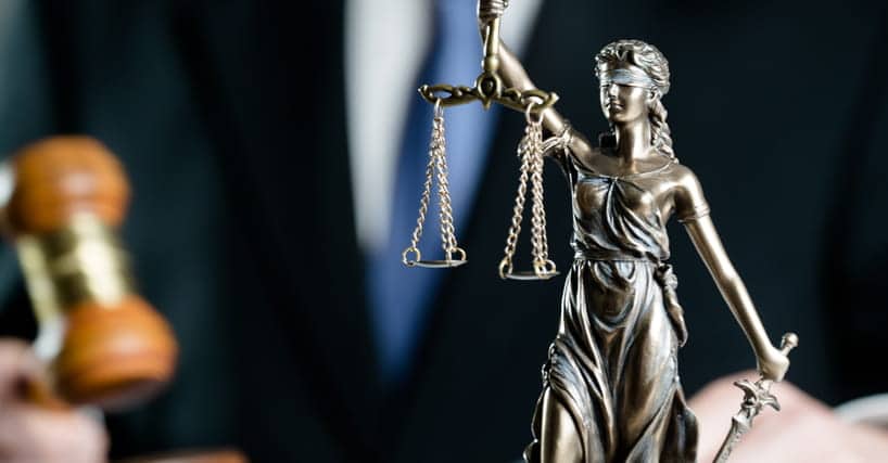 A Lady Justice statue with a car accident attorney holding a gavel blurred out in the background representing car accident injury law