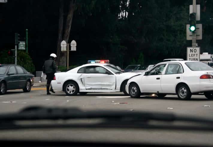 A cop inspecting a car accident at an intersection. 