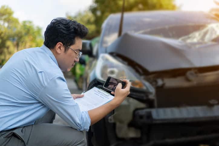 An insurance adjuster taking photos of a damaged vehicle after an accident. 