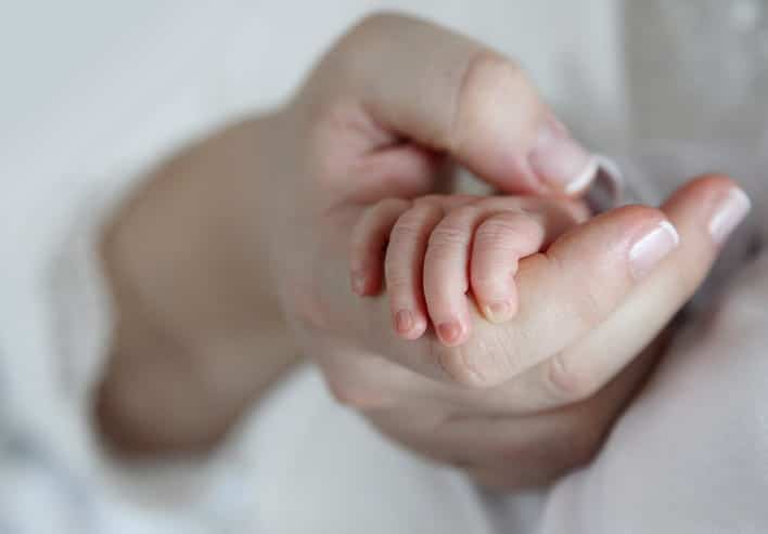 A mother holding the hand of her newborn. 