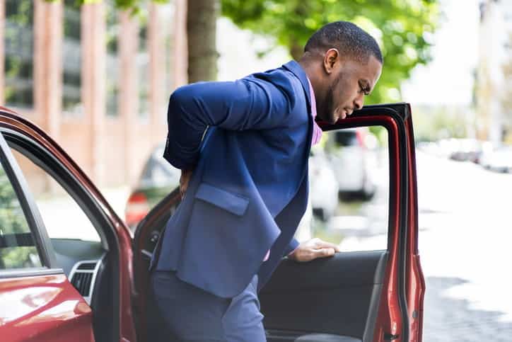 A man is holding his back in pain as he exits the vehicle after a car accident. 