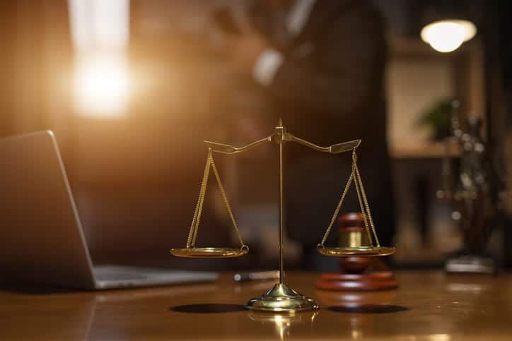 The scales of justice in front of a gavel and an open laptop on a car accident lawyer's desk. 