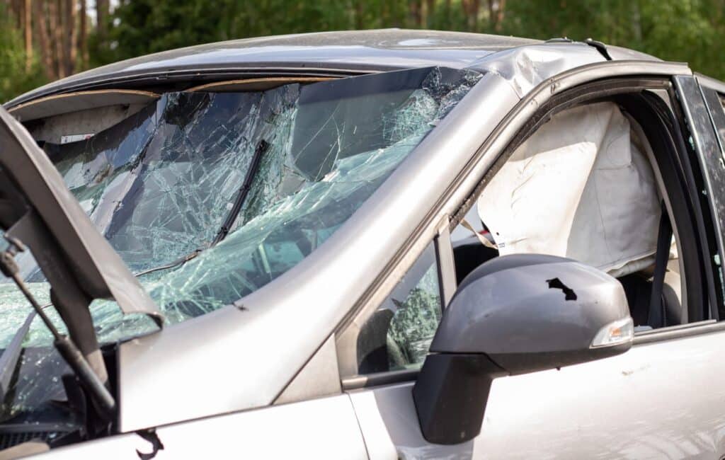 An up-close view of the damage to a vehicle after being in a car accident. The airbag is deployed, and the windshield is smashed.